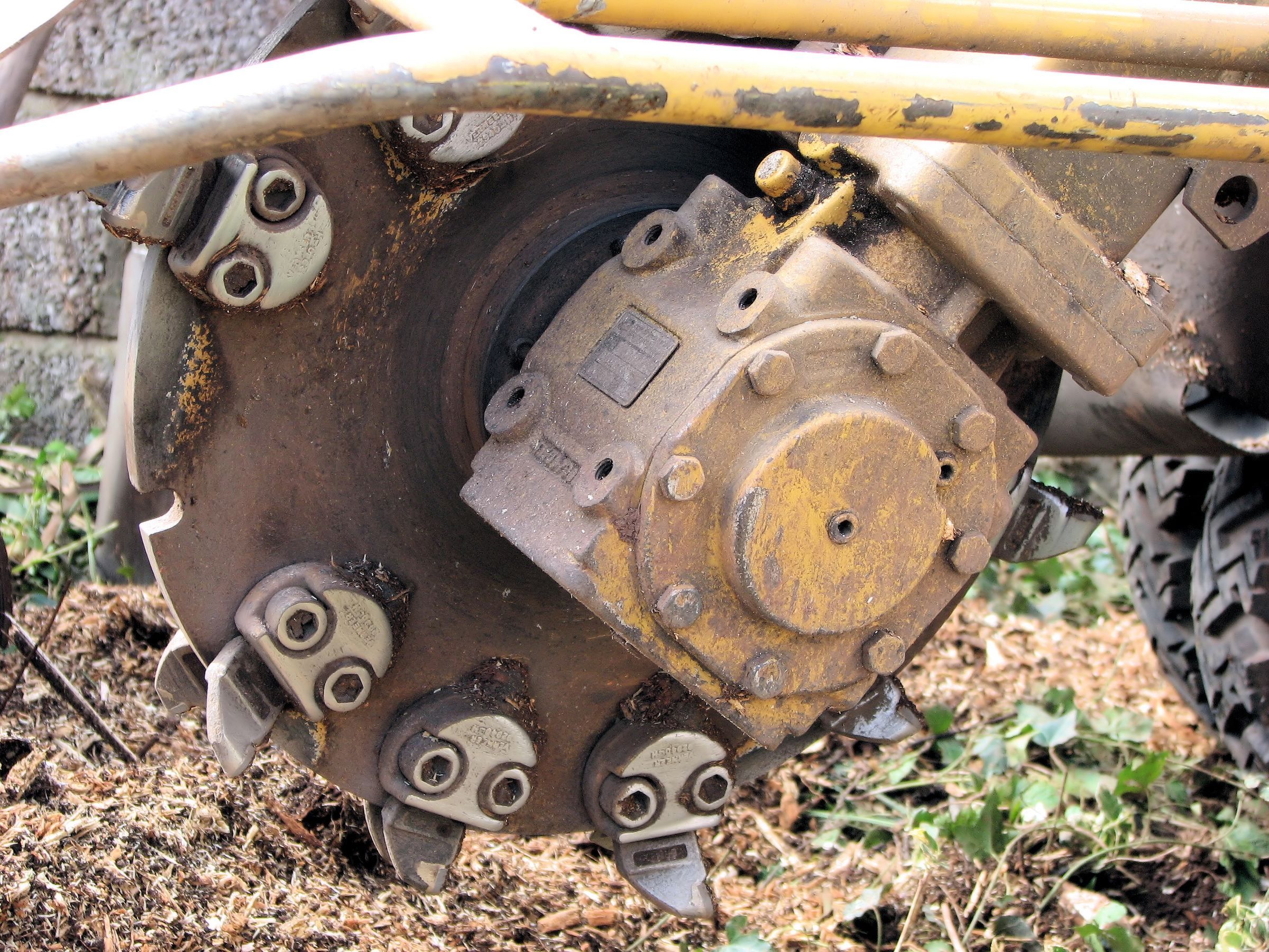 Close view of a stump grinder cutting wheel with bolted carbide teeth, at rest on wood chips.